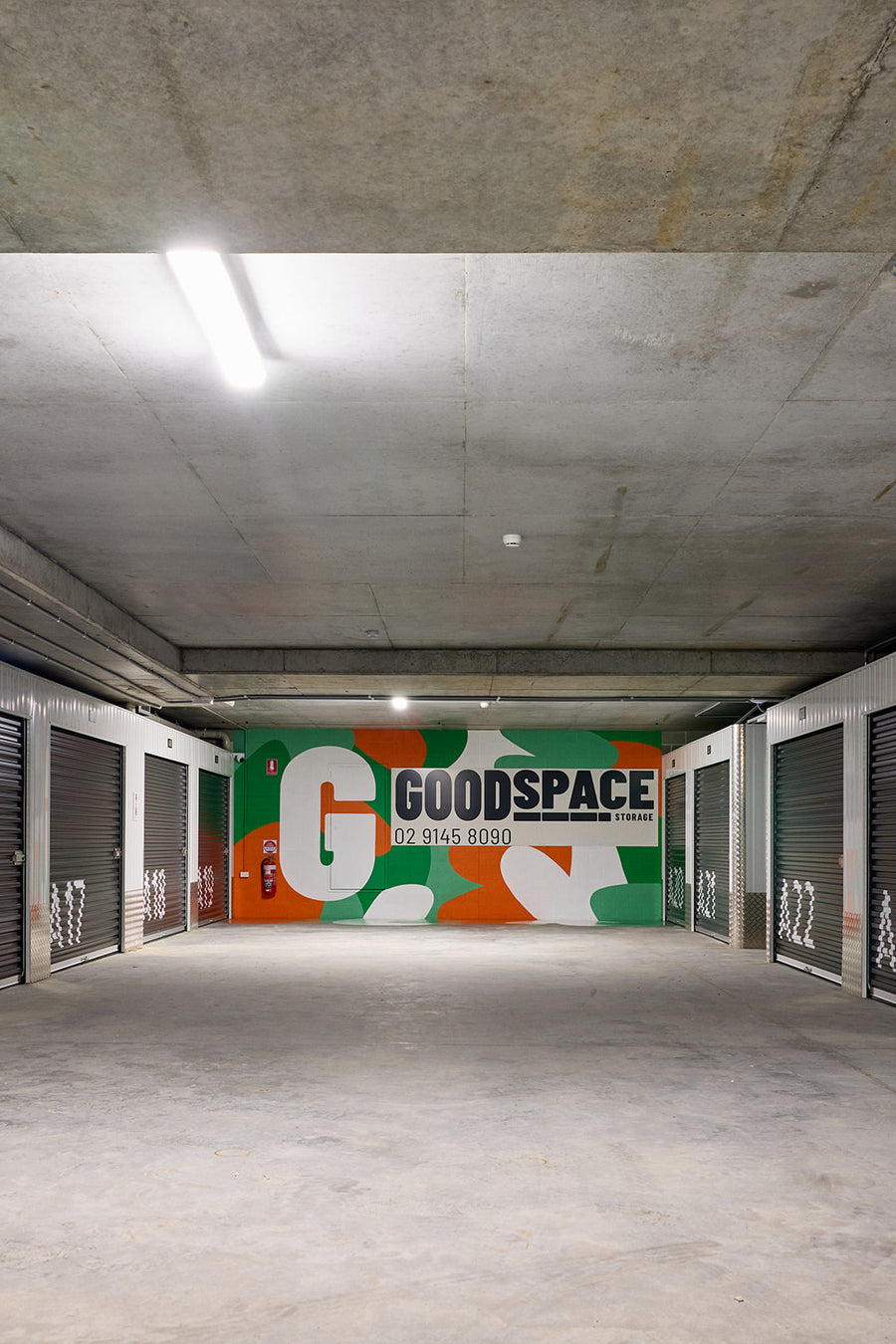 Corridor of roller-door storage units at Goodspace Rouse Hill with a bright orange and green Goodspace mural on the end wall